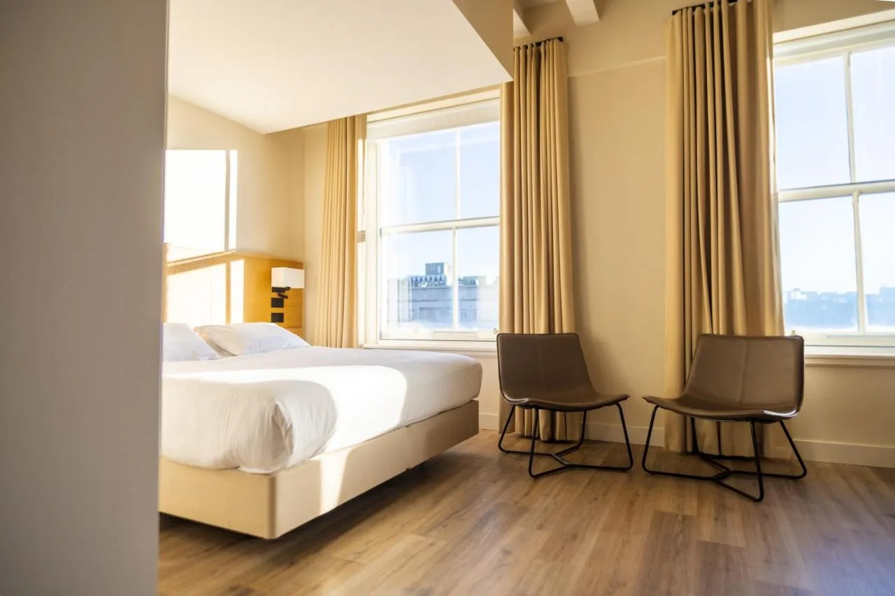 a bedroom with a bed and two chairs and windows at School Lane Hotel in Liverpool ONE in Liverpool